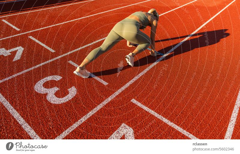 Runner in starting position on a red track, sunlight casting shadow, athletic gear, fitness athlete starting block race track and field sprinter competition