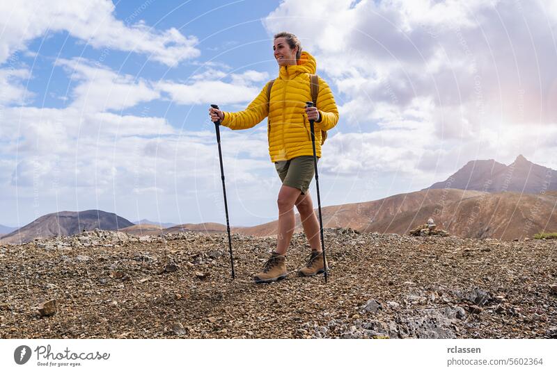 Hiker in yellow jacket with trekking poles on a rocky mountain trail, mountains in the back fuerteventura hiker hiking outdoor adventure nature active lifestyle