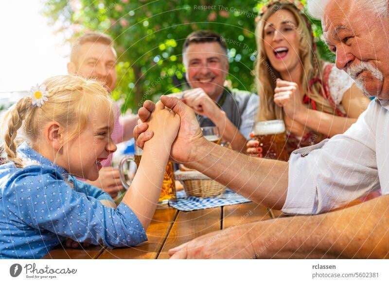 Bavarian family practicing the high art of arm wrestling in a beer garden grandfather daughter kid child gambling cheer on pretzels game friends woman senior