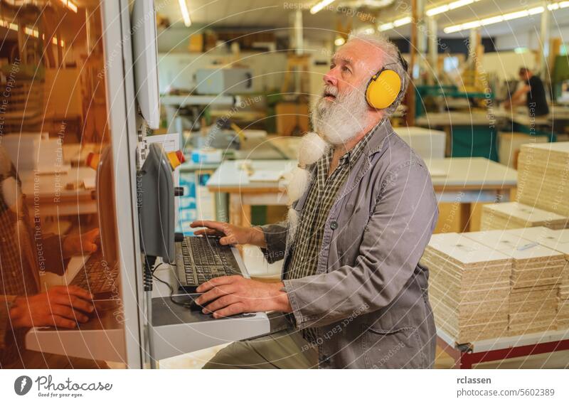 Man using computer on a cutting machine in a woodworking workshop earmuffs professional craftsman workbench furniture industry hearing protection industrial