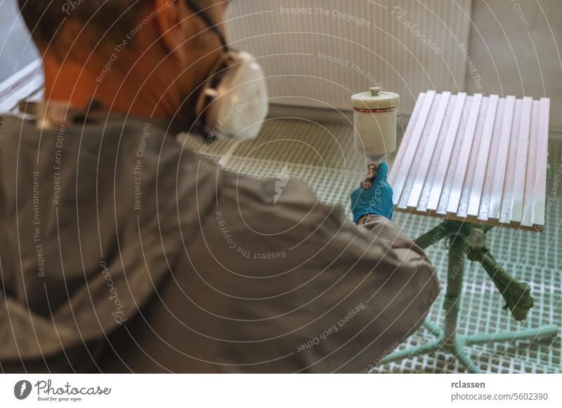 Person in protective clothing spray painting a wodden panel with a window in the background carpenter craftsman mask spray gun painter wooden panel workshop