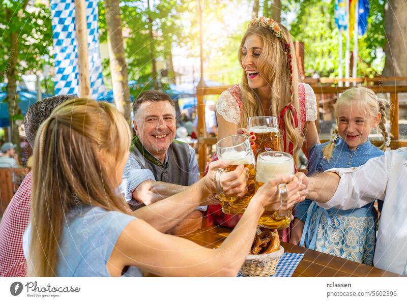 friends and family in Tracht, Dirndl and Lederhosen having fun sitting on table drinking beer and eating pretzels in Beer garden or oktoberfest in Bavaria, Germany