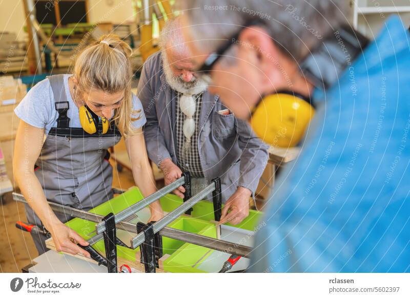Three carpenters with ear protection working on a clamped wood piece in a workshop teamwork professional craftsman workbench furniture industry worker