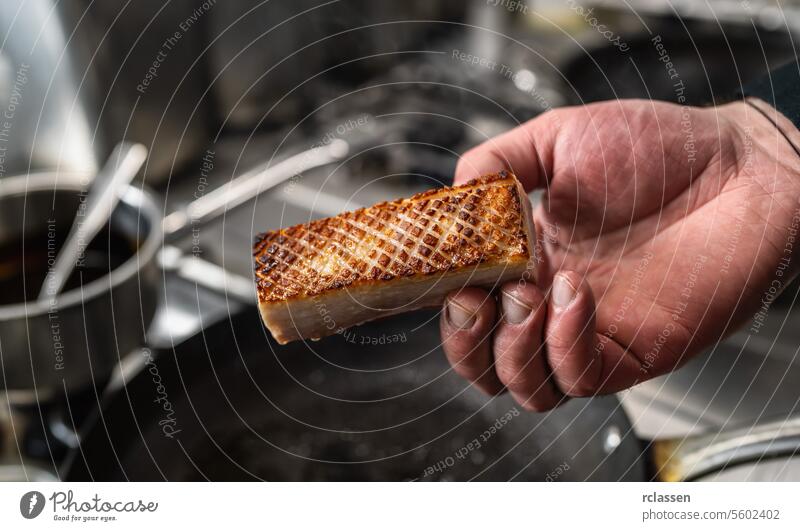Hand holding a Crispy pork belly which was roasted in a hot pan in a professional kitchen at a restaurant. Luxury hotel cooking concept image. hand crust
