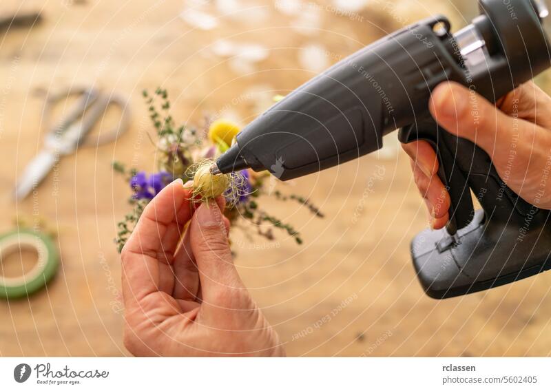 Hands using a glue gun on a small floral craft project hands diy handmade crafting tools creativity hot glue art design hobby flower arrangement decoration