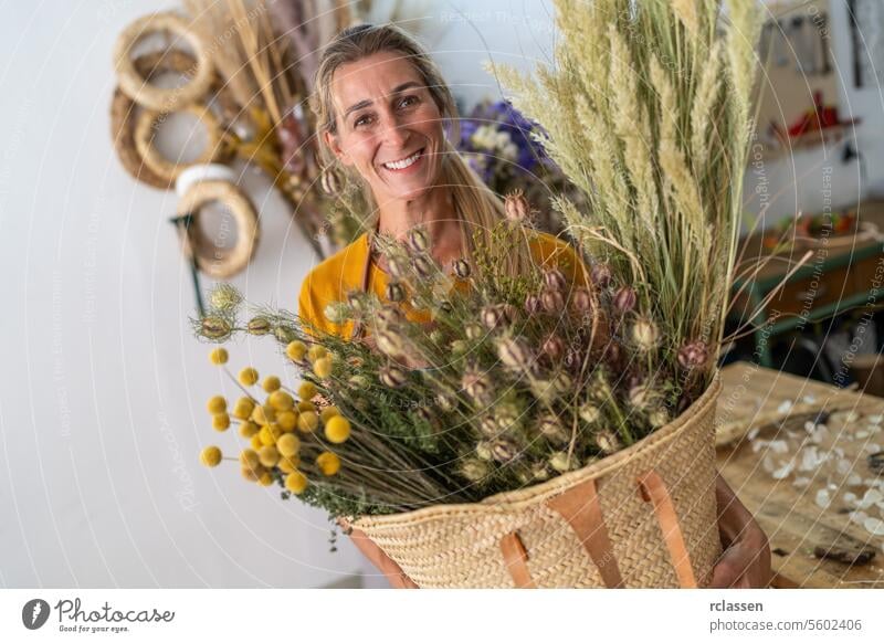 Radiant female florist holding a large basket of dried flowers in her studio radiant florist studio smiling happy floristry natural bouquet crafting