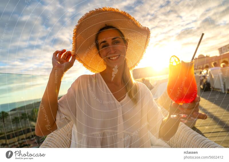 Joyful woman in straw hat offering a cocktail at tropical beach hotel with sunset in the background paradise beach playa coastline canary island joy vacation