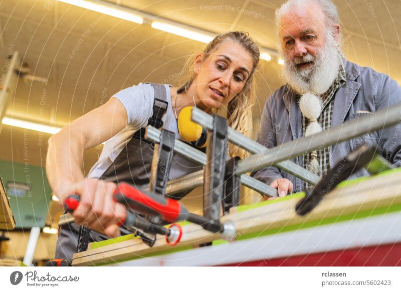 Master carpenter and apprentice using a clamp for wood gluing in a workshop professional craftsman workbench furniture industry worker wooden timber carpentry