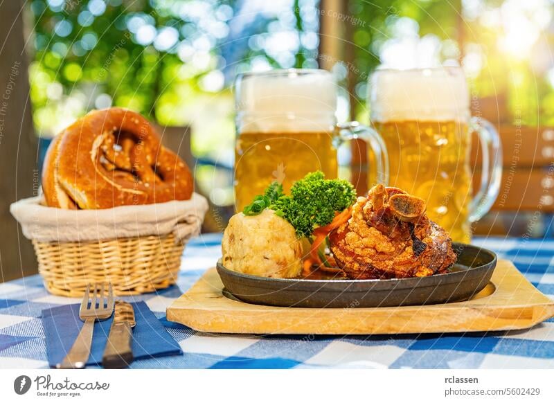 Schweinshaxe, traditional Bavarian cuisine with roasted ham hock (pork knuckle) with potato dumpling, brezen and beer mug on a table at beer garden or oktoberfest