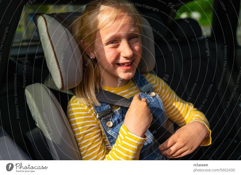Happy girl in casual clothes looking at camera buckle up while sitting on back seat of car during road trip sunlight scarecrow smiling backseat blond daughter