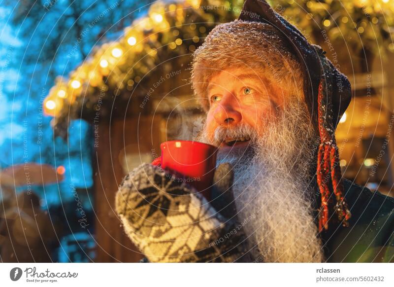 Smiling man with a beard holding a red mug of Mulled wine or hot chocolate at a Christmas market, festive lights in background punch tourist merry christmas cup