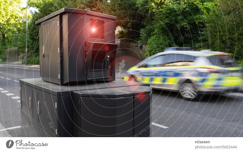 Speed camera on roadside with a police car passing by in motion blur, trees in background speed camera law enforcement traffic safety vehicle speed surveillance