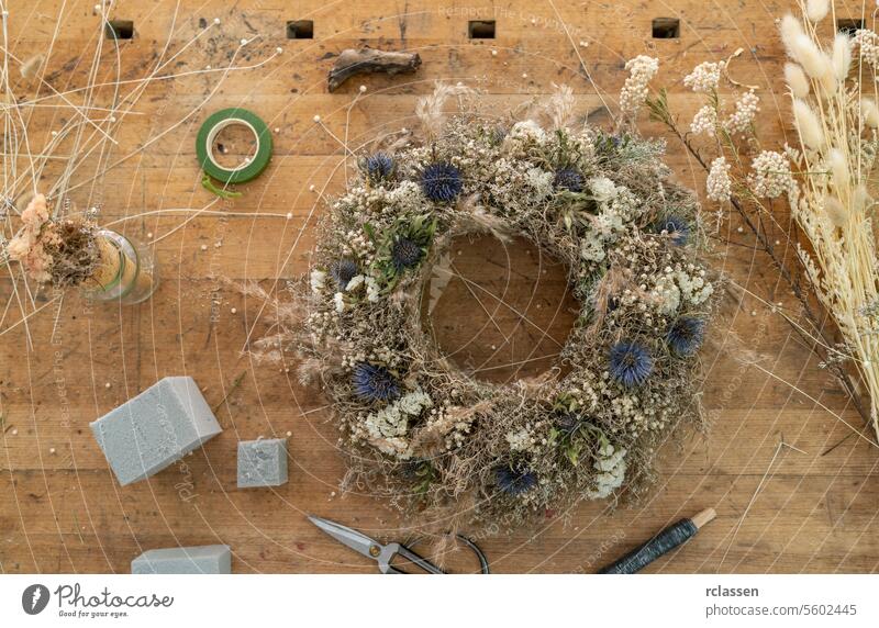 Overhead view of a floral wreath on a wooden table among florist tools and crafting materials overhead view dried flowers workshop diy handmade creative