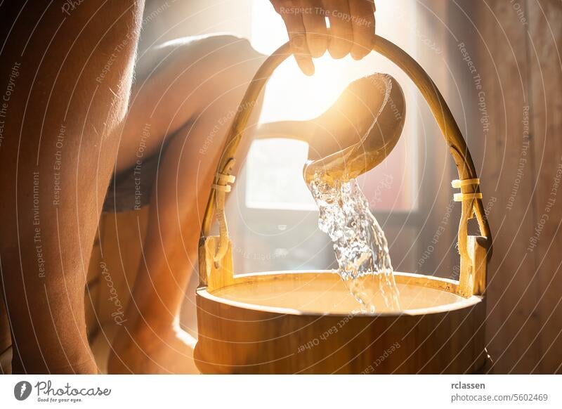pouring water out of a wooden bucket in the Finnish sauna, spa and Warm temperature bath therapy concept image. scroop mist splash sunlight hand steam finnish