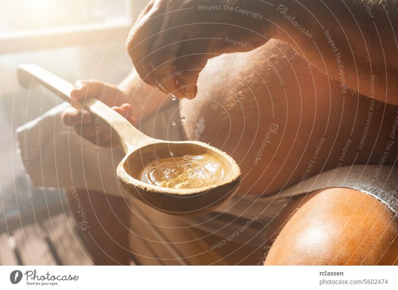 Old man dripping water in to a old wooden spoon in the Finnish sauna, spa and Warm temperature bath therapy concept image. drop belly scroop mist splash