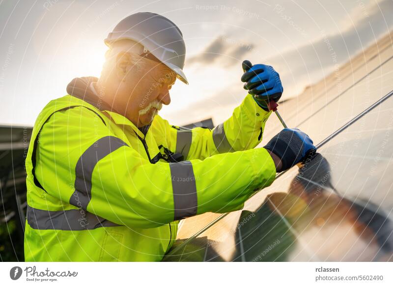 engineer using a screwdriver to  assembling a solar panel in a solar park at sunset. Alternative energy ecological concept image. technology plant industry