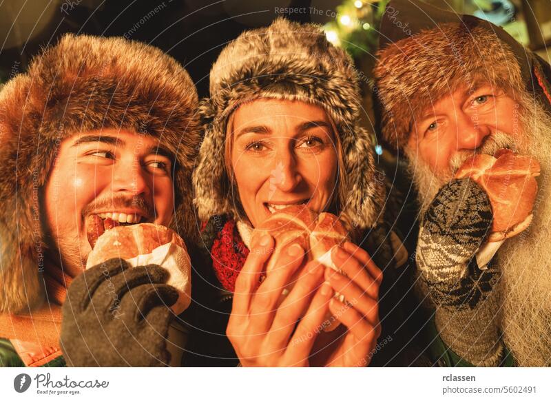 Group of friends enjoying sausages in bread rolls at a lively Christmas market, with winter hats and smiles. merry christmas gloves traditional mulled wine