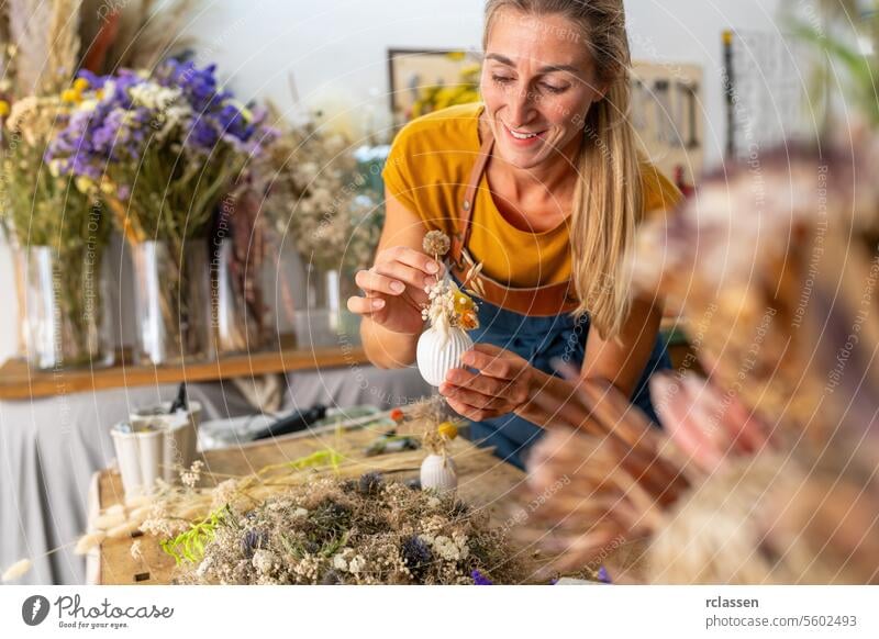 female florist arranging a small white vase with dried flowers in a bright workshop smiling crafting floristry decoration handmade diy creativity yellow top