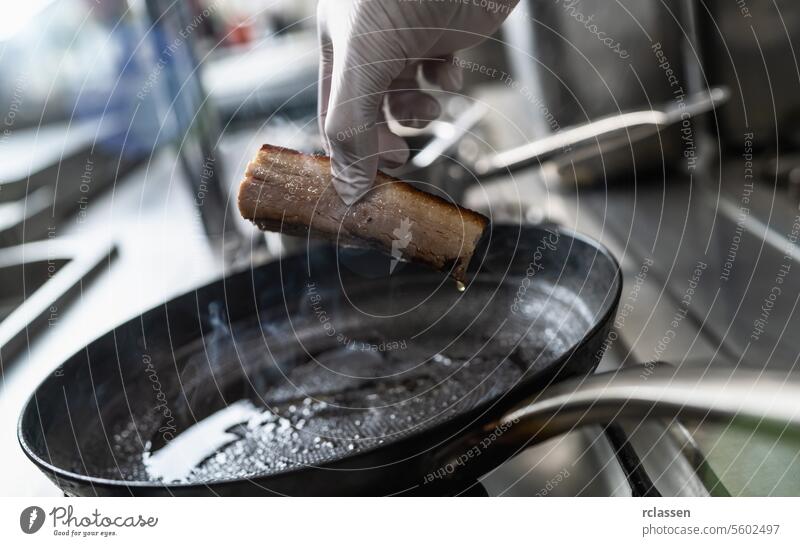 Hand holding a Crispy pork belly which was roasted in a hot oiled pan at a gas stove in a professional kitchen at a restaurant. Luxury hotel cooking concept image.