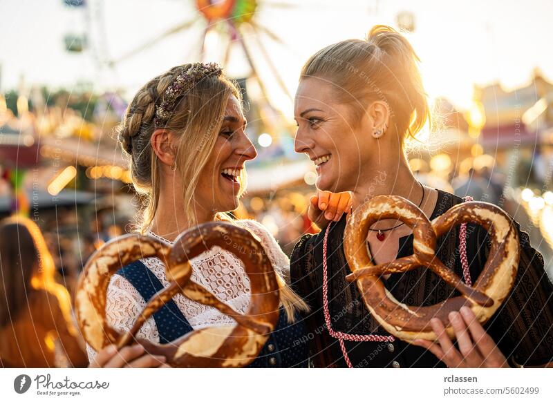 girlfriends look at each other  holding pretzel or brezen on a Bavarian fair or oktoberfest or duld in national costume or Dirndl in germany woman party