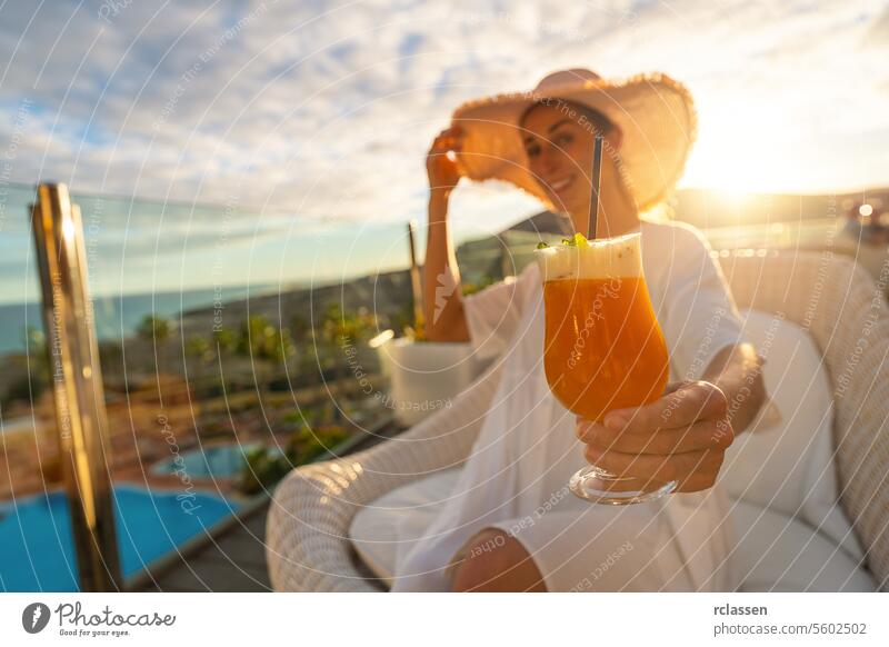 Woman in a sun hat enjoying a cocktail at tropical beach hotel on a sunny terrace with a pool in the background paradise beach playa coastline canary island