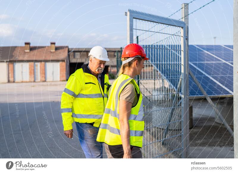 Male and female engineers at a solar power plant gate to inspection check discussion high-visibility vests safety helmets industrial site renewable energy
