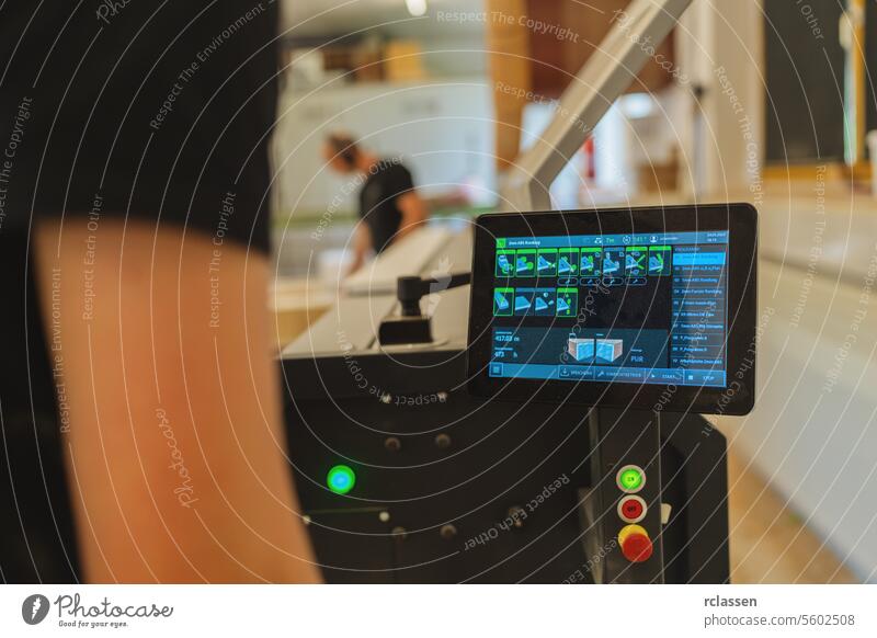 Touchscreen control panel of machinery with workers in background at a workshop touchscreen carpentry woodworking industrial technology equipment manufacturing