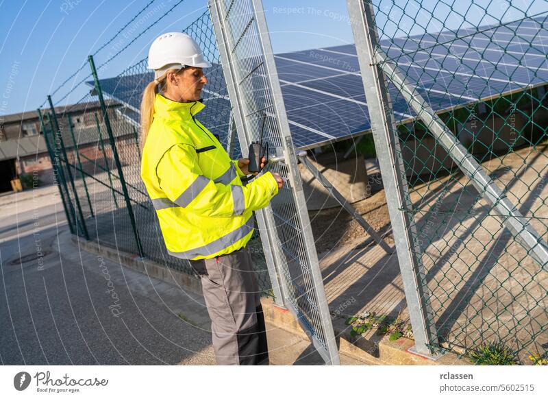 Technician in high visibility jacket on a gate with walkie-talkie at solar farm. Alternative energy ecological concept image. renewable resource technology