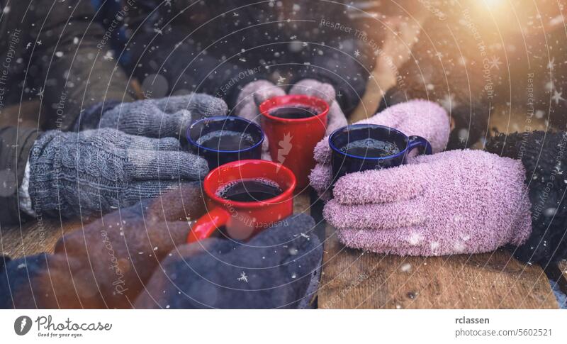 Mugs of mulled wine on a table surrounded by gloved hands in snow punch christmas market advent german merry christmas cup hot chocolate mugs warm drinks