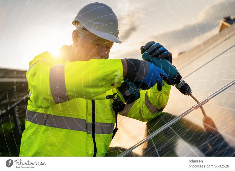 Engineer using a drill for solar panel installation at sunrise. Alternative energy ecological concept image. technology plant industry electricity worker adult