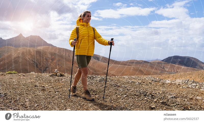 Hiker in yellow jacket with trekking poles on a mountain trail under a cloudy sky fuerteventura hiker adventure hiking nature outdoors active lifestyle