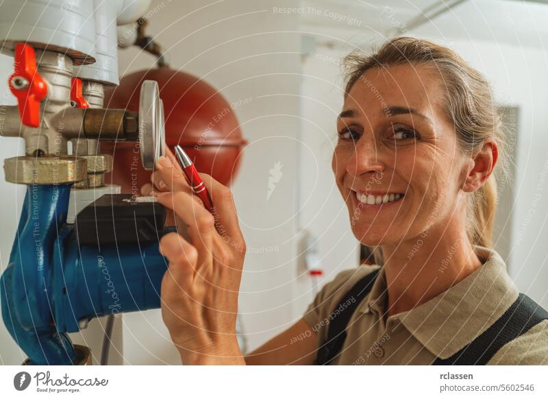Happy female heating engineer checks gas thermostat at a boiler room with a old gas heating system. Gas heater replacement obligation concept image read