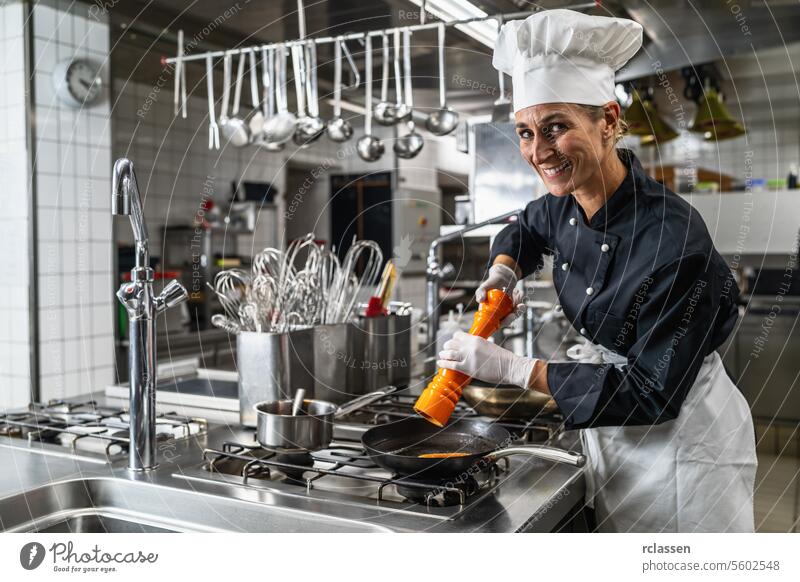 Smiling female chef in hotel or restaurant kitchen cooking and seasoning the food with a pepper or salt mill pepper mill spice smiling uniform grinder woman