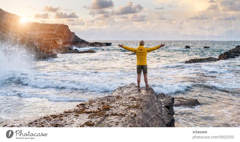 Person in yellow jacket standing on rock by the sea with arms wide open at sunset fuerteventura freedom nature person coastline rocks waves open arms adventure