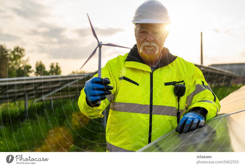 Senior engineer holding a wind turbine model at a solar photovoltaic panel system at sunset. Alternative energy ecological concept. technology industry