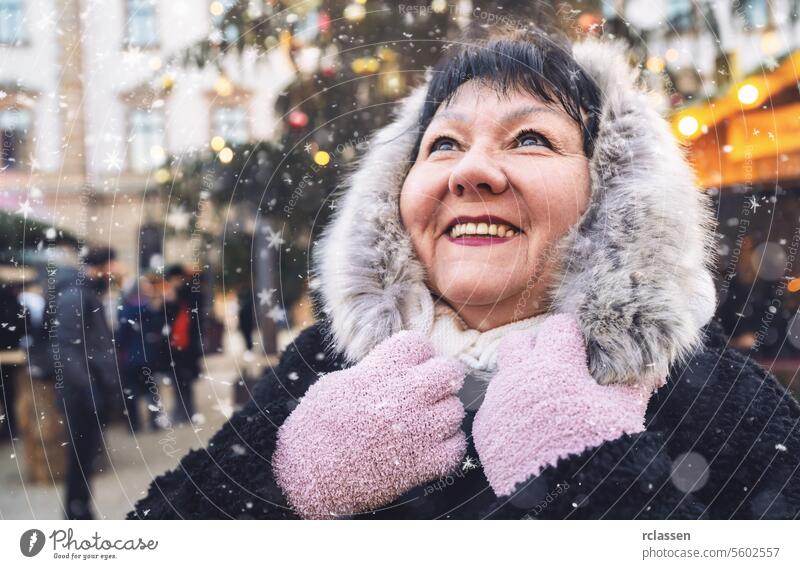 Elderly woman smiling at a winter Christmas market, with snow falling, in festive attire happy merry christmas hot chocolate gloves traditional mulled wine