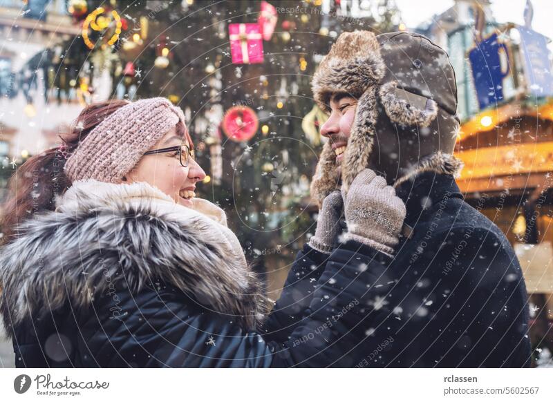 Couple in winter attire smiling at each other, at a snowy winter day at a christmas market friends mulled wine boyfriend beard tourism dating fair travel happy
