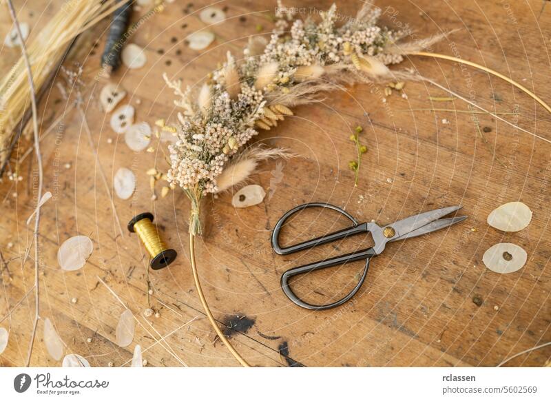 Dried flower arrangement and scissors on a wooden table with scattered petals and thread spool workshop lunaria dried flowers floristry diy rustic natural