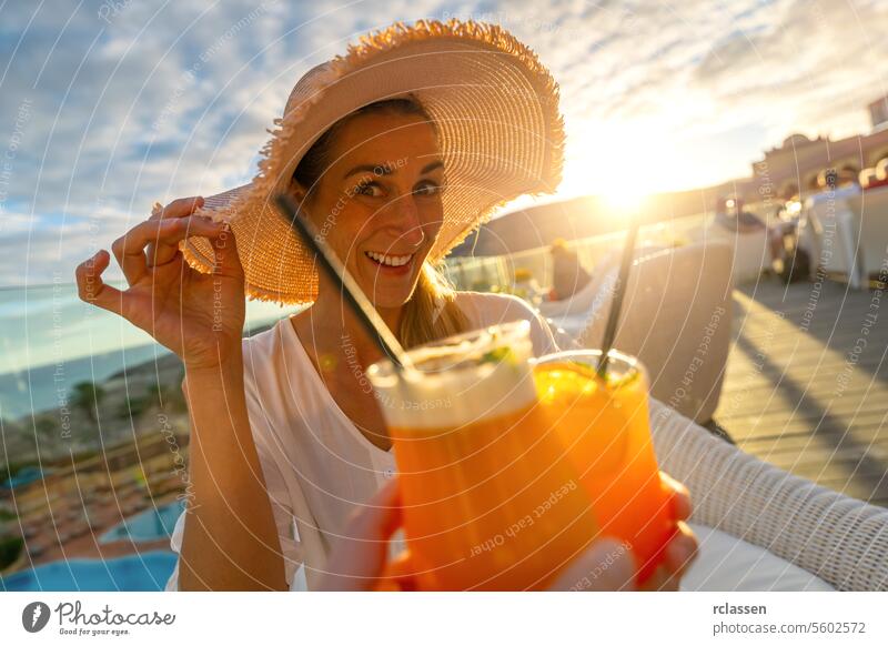 Woman in sun hat smiling and toasting with a cocktail at tropical beach hotel on sunset with blurry background paradise beach playa coastline canary island