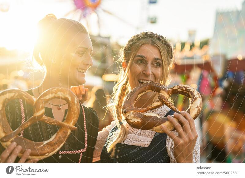 Girlfriends together on a Bavarian fair or oktoberfest or duld in national costume or Dirndl eating pretzel or brezen woman party beergarden dirndl girlfriends