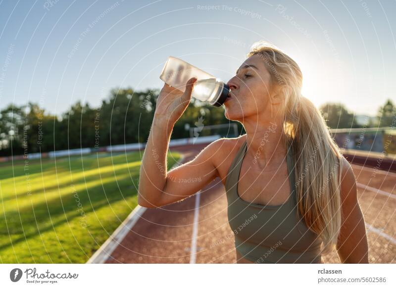 Athlete woman drinking from a water bottle on a track field athlete fitness hydration health wellness sportswear sunset exercise outdoor active wear training