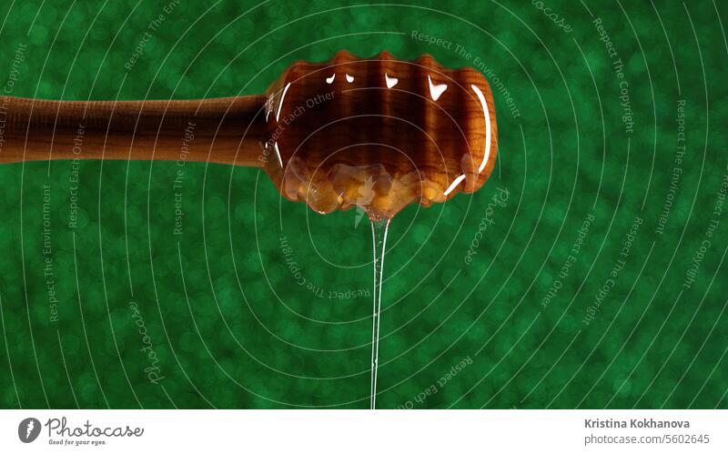 Organic honey flows from wooden dipper stick on green background. Apiary closeup dessert food golden healthy ingredient liquid sweet bee drop fresh natural