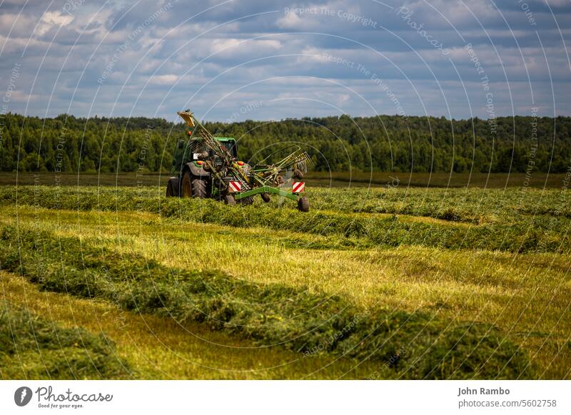 green haymaking tractor on summer field before storm - telephoto shot meadow country rural light agricultural day farm machinery agriculture harvesting farming