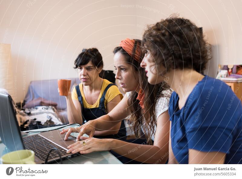 Three focused women collaborate over a laptop in a home setting, epitomizing the dynamics of a contemporary remote work team Teamwork Women Collaboration Laptop