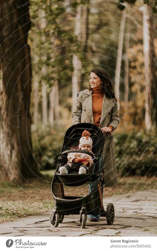 Young woman with cute baby girl in baby stroller at the autumn park adorable adult care caucasian child childhood daughter fall family female foliage happiness
