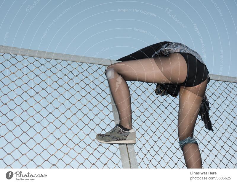 A wild girl is climbing a fence fiercely. Her sexy black panties and long legs are the main subject of this image. However, the feeling that there is an ongoing riot is also there.