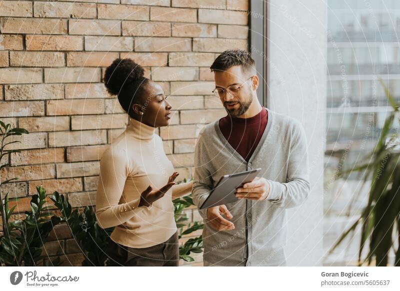 Young multiethnic business couple with digital tablet standing and discussing in the modern office adult african american black businessman businesspeople