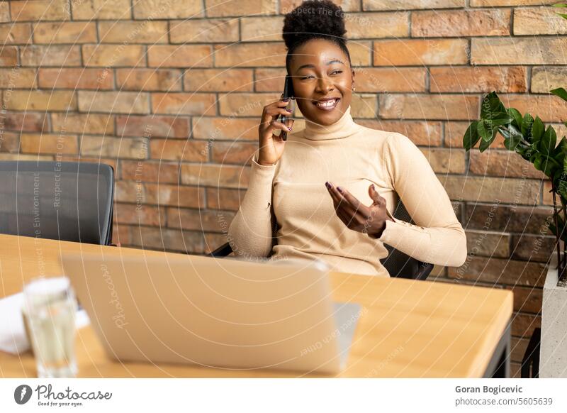 One young African American business woman using mobile phone while sitting by the brick wall in the industrial style office adult african american black