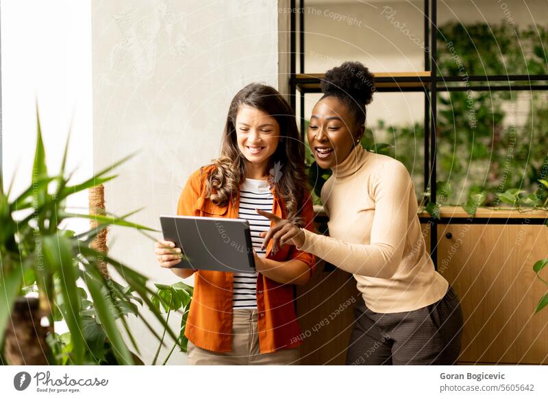 Two young business women with digital tablet standing in the modern office adult african american black businessman businesspeople businesswoman businesswomen