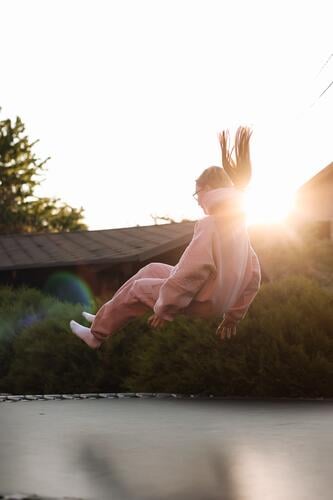 Happy little child girl having fun and jumps on trampoline outdoors, at backyard of the house on sunny summer day, active recreation on summertime vacation. Happy childhood concept. Children's day.